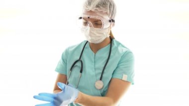 Tıbbi maske ve güvenlik gözlüğü takan kadın doktor tek kullanımlık eldiven takıyor. Sağlık çalışanlarının bireysel koruması.