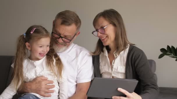 Dítě a prarodiče užívají PC tabletu. Milující pár středního věku a jejich vnučka používají doma digitální tablet. Senioři a moderní technologie.