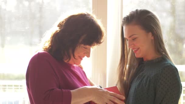 Älskade vuxna dotter presentera våren blommor till glad gammal mor skrattar bonding omfamnande, ung kvinna gratulera kramar medelålders mamma. Mammas dag hemma — Stockvideo