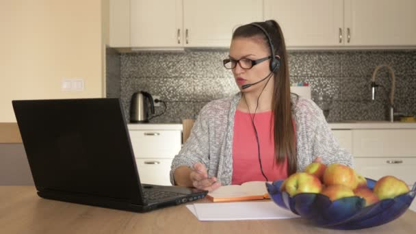 Mujer joven con auriculares delante de la computadora portátil en la mesa, consulta al cliente en línea . — Vídeo de stock