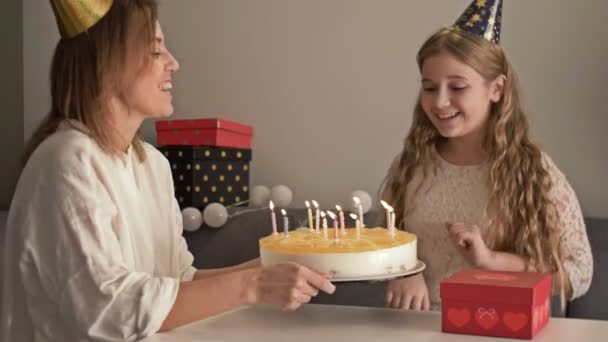 Beautiful mother and her teenager daughter are celebrating a birthday. Mom and child are blowing on candles on cake — Stock Video