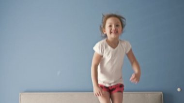 Mutlu küçük kız yatakta zıplarken eğleniyor.