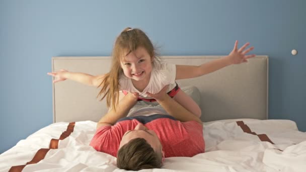 Padre joven criando a su hijita, jugando juntos en la cama en casa, concepto de paternidad . — Vídeos de Stock