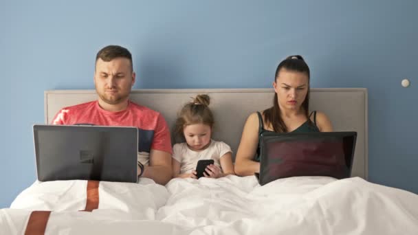 Le matin du jour de congé en famille. Maman, papa et l'enfant sont couchés au lit. Ils ont un passe-temps commun. Chacun garde son gadget . — Video