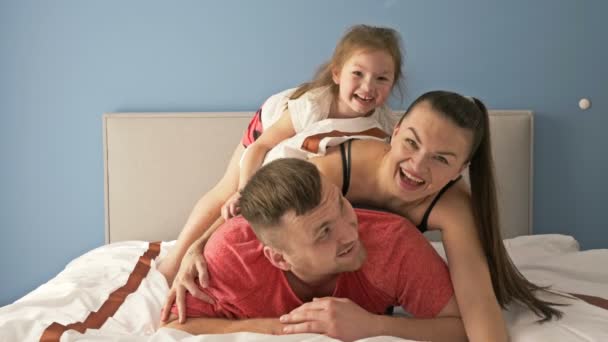 Eğlenceli aile sabahı. Baba, anne ve küçük kız yatakta oynuyorlar.. — Stok video