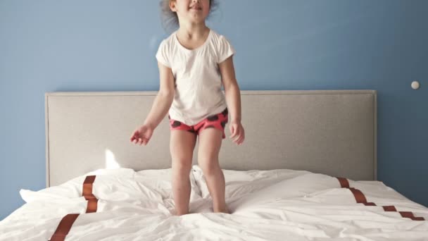 Niña juguetona divirtiéndose saltando en la cama . — Vídeos de Stock