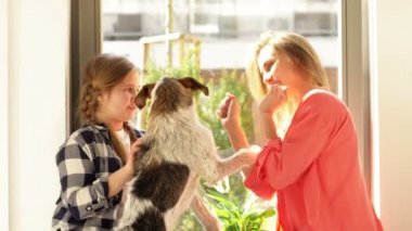 Genç bir kadın ve kızı köpeğiyle pencerede oyun oynuyorlar..