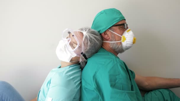 Tired doctor and a nurse are sleeping, sitting back to back on the floor. — Stock Video