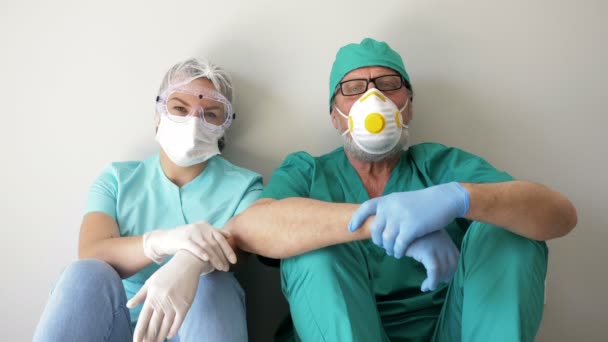 Médico y enfermera cansados están descansando sentados en el suelo en un pasillo del hospital . — Vídeos de Stock