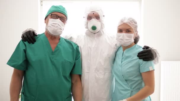 Tres doctores de pie abrazando. Demuestran que todo saldrá bien. Covid-19 . — Vídeos de Stock