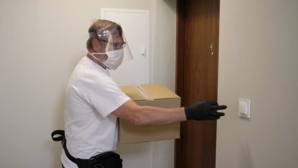 Mensajero en una máscara protectora y guantes entrega un paquete, una mujer joven en una máscara médica recibe una caja. Servicio de entrega en cuarentena . — Vídeo de stock