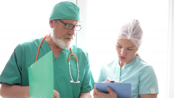 Een bejaarde arts wijst een jonge verpleegster de weg. — Stockvideo