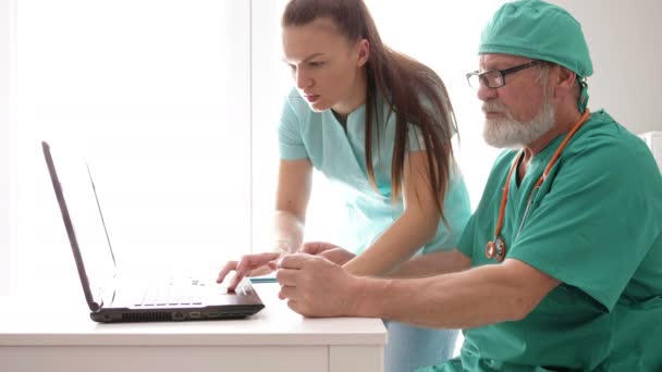 Médico sênior e jovem enfermeiro examinam dados de pacientes em banco de dados de computadores hospitalares . — Vídeo de Stock