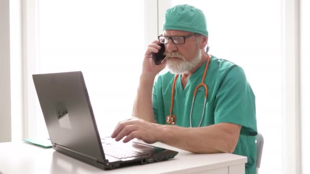 Medico senior in ufficio lavora su un computer e parla di telefono cellulare . — Video Stock