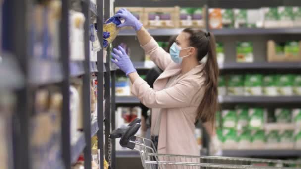 Süpermarkette alışveriş yaparken koruyucu maske ve eldiven takan bir kadın. Coronavirus salgını kavramından korkuyor. — Stok video