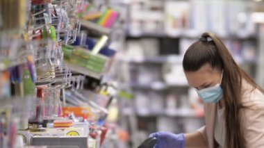 Koruyucu maske takan ve eldiven takan alışverişçi kadın süpermarkette kırtasiyeyi inceliyor. Covid 19.