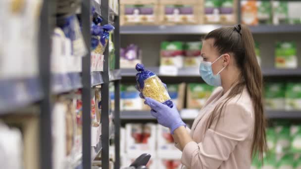 Kvinna i skyddsmask och handskar väljer pasta i en stormarknad. Shopping under Covid-19-epidemin. — Stockvideo