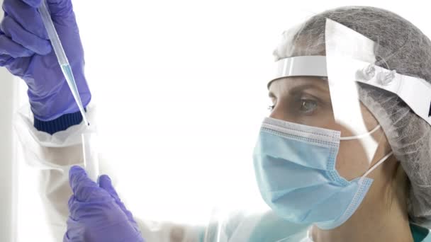 Portret van een vrouwelijke laboratoriumassistent in een beschermend pak met een pipet. Close-up. — Stockvideo