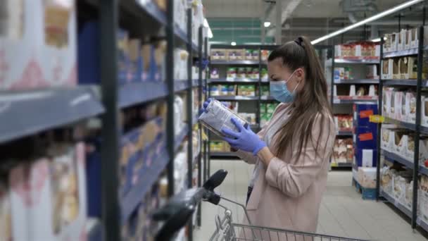 Jeune femme en masque protecteur et gants choisit des pâtes dans un supermarché. Shopping pendant l'épidémie de Covid-19 . — Video