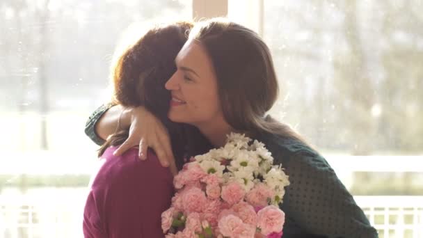 Jovem mulher adulta filha abraçando feliz mãe de meia-idade, abraçando a ligação parabenizando a mãe madura com o conceito de dia das mães, apresentando flores, comemorando juntos — Vídeo de Stock