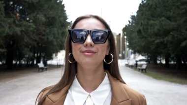 Güneş gözlüklü genç bir kadın şehir parkında yürüyor. Bahar. Bahar havası.