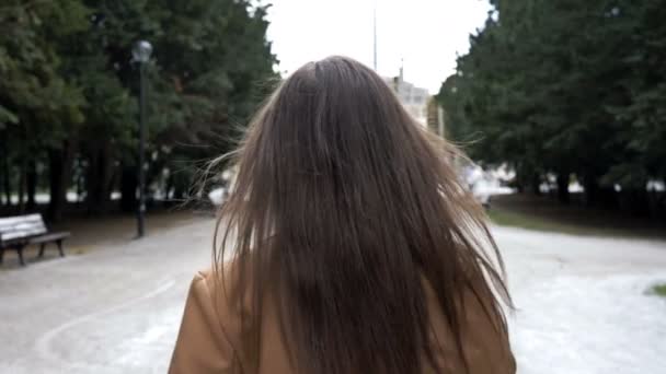 Chica atractiva caminando por el callejón del parque de la ciudad mira a su alrededor con una sonrisa . — Vídeos de Stock