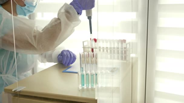 Krevní testy v laboratoři. Laborant v ochranném oděvu pracující s dávkovačem. — Stock video