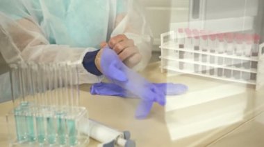 Masada oturan laboratuar teknisyeni koruyucu lateks eldivenler giyer. Çalışmaya hazırım..