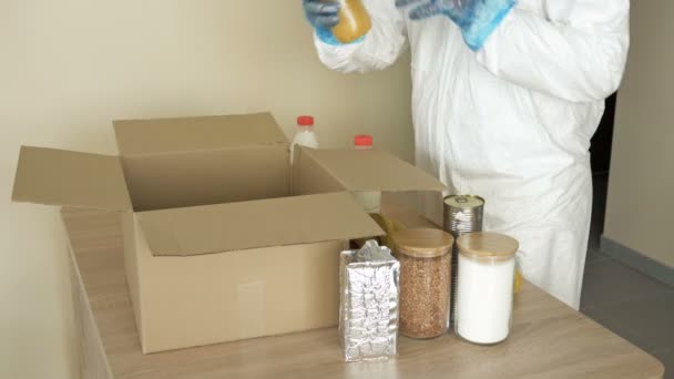 Voluntario en ropa protectora pone comida en una caja. Para personas en situaciones difíciles debido a la epidemia de covidio-19 . — Vídeos de Stock