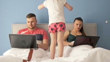 Evde internet işi. Yatakta yatarken dizüstü bilgisayarlarla çalışan genç evli bir çift. Küçük kız çok sıkılmış, ebeveyn ilgisine ihtiyacı var..