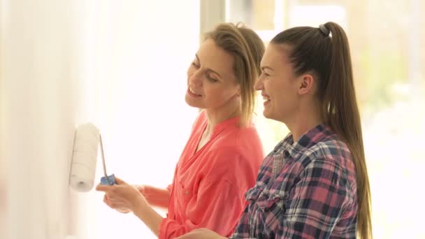Duas belas mulheres ativas jovens alegremente pintura parede com rolos de tinta . — Vídeo de Stock