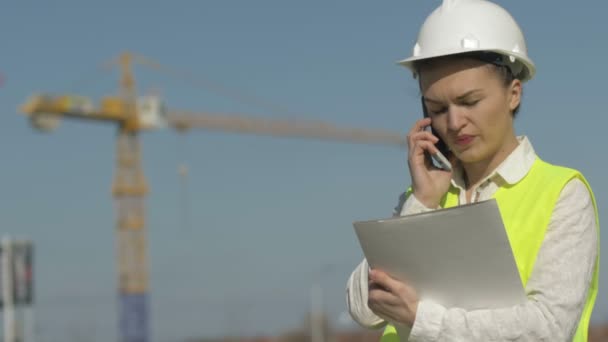 Builder kvinna i en hjälm har en mapp med dokument och samtal på telefonen. Framgångsrik affärskvinna. — Stockvideo