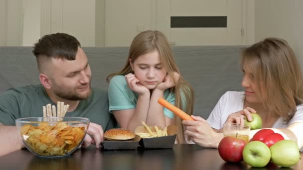 Elk familielid heeft zijn eigen smaak. Papa eet met plezier fastfood, mama is vegetariër. vrouw wil haar dochter naar eten groenten en fruit. — Stockvideo
