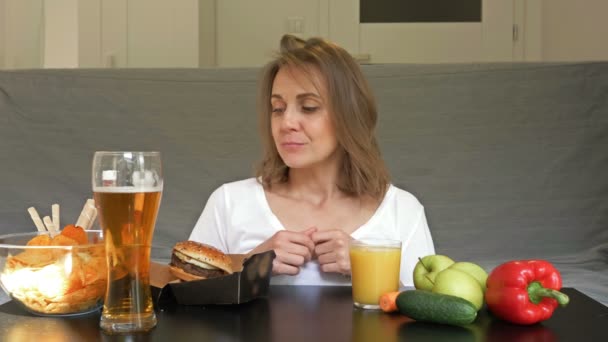 Smal vacker kvinna vet inte vad hon föredrar att äta. Svårigheten att välja mellan hälsosam och ohälsosam kost. — Stockvideo