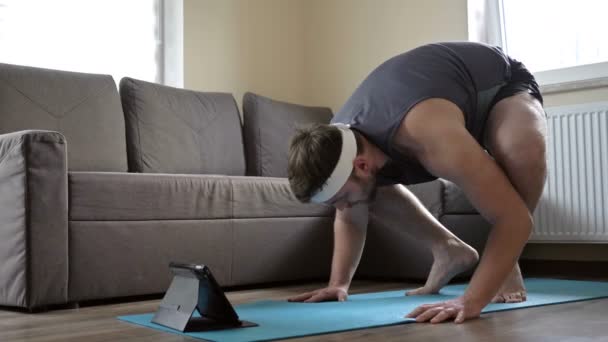 Mladý muž se snaží dělat komplexní sportovní cvičení. Sportování on-line doma. — Stock video