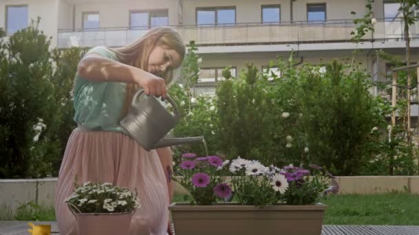 Mignon adolescent fille arrosage fleurs dans un pot à partir d'un arrosoir dans son maison jardin . — Video