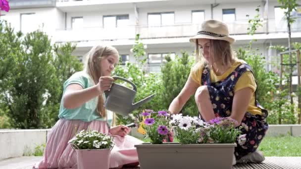 Madre e hija adolescente plantaron flores en maceta en el patio de su casa. Chica está regando flores de una regadera, mujer está sonriendo . — Vídeo de stock