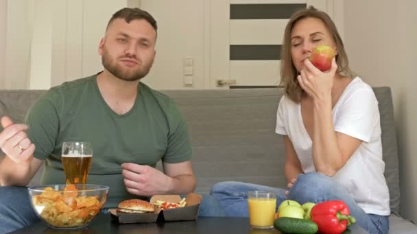 Casal jovem tem hábitos alimentares diferentes. O marido está feliz em comer fast food, a esposa é vegetariana. Dieta saudável e não saudável . — Vídeo de Stock