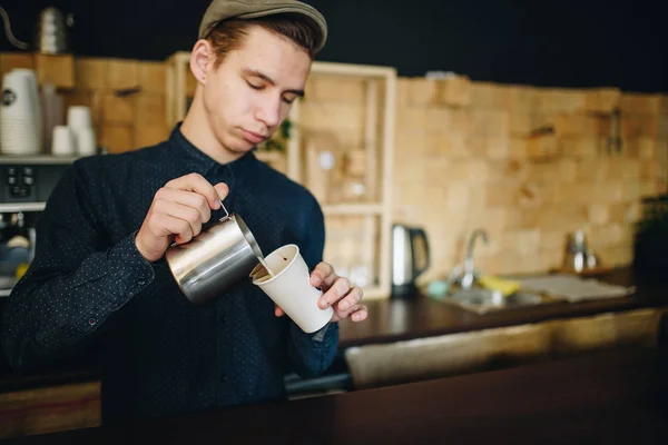 Man barista prepares delicious coffee near the wall construted is small desk squares