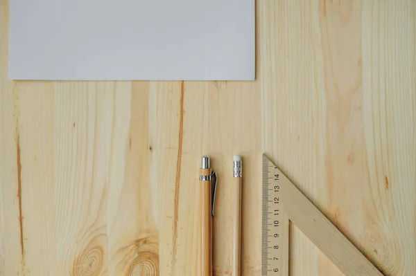 Carta bianca, matita, penna, triangolo sulla scrivania in legno alla luce del giorno — Foto Stock