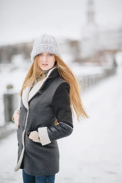 Молода красива щаслива усміхнена дівчина позує на вулиці. Модель грає з її довгим волоссям, торкаючись обличчя. Жінка в стильному одязі. Концепція зимових свят. Ефект магічного снігопаду — стокове фото