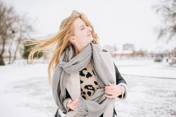 Young beautiful happy smiling girl posing on street. Model playing with her long hair, touching face. Woman wearing stylish clothes. Winter holidays concept. Magic snowfall effect — Stock Photo, Image