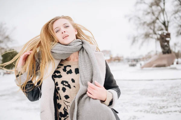 Joven hermosa chica sonriente feliz posando en la calle. Modelo jugando con su pelo largo, tocando la cara. Mujer vestida con ropa elegante. Concepto de vacaciones de invierno. Efecto mágico nevada —  Fotos de Stock