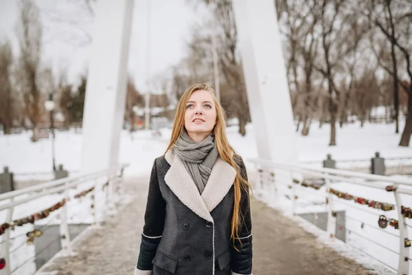 Joven hermosa chica sonriente feliz posando en la calle. Modelo jugando con su pelo largo, tocando la cara. Mujer vestida con ropa elegante. Concepto de vacaciones de invierno. Efecto mágico nevada — Foto de Stock