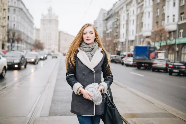 Unga vackra glada leende flicka poserar på gatan. Modell spelar med hennes långa hår, röra vid ansiktet. Kvinna som bär snygga kläder. Vinter semester koncept. Magiska snöfall effekt — Stockfoto