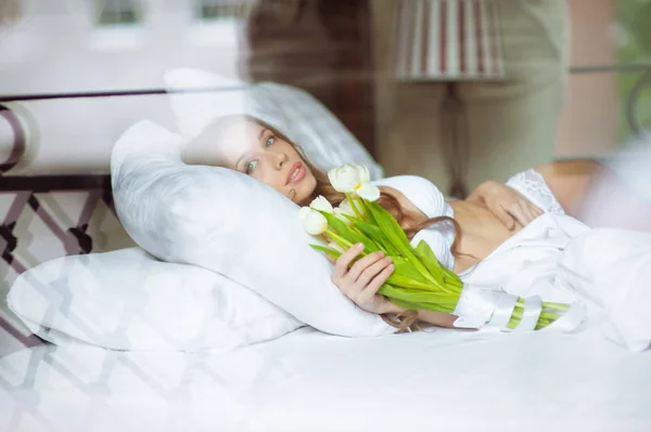 Vackra brud i sexiga underkläder ligger på en säng med bukett blommor. Sexuella minnen — Stockfoto
