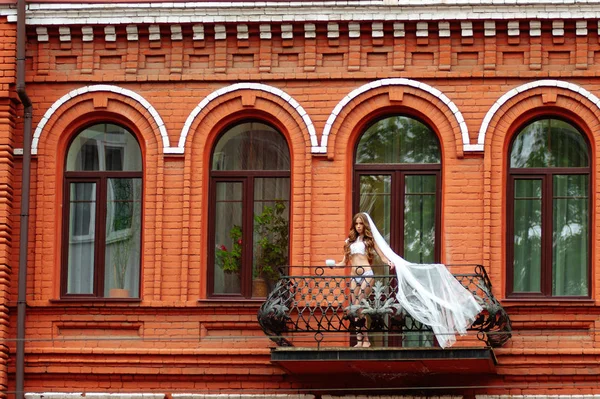 Braut in sexueller Dessous mit Tasse Kaffee auf Balkon des Luxus-Appartements im roten Hotelgebäude. — Stockfoto