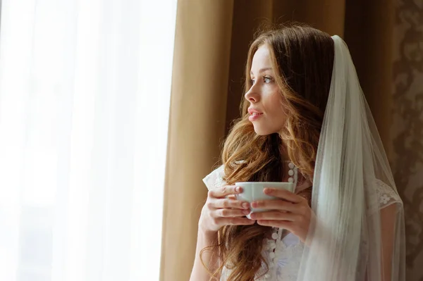Bruden i sexuella underkläder med kopp kaffe nära windiw av lägenhet på röda hotellbyggnaden. — Stockfoto