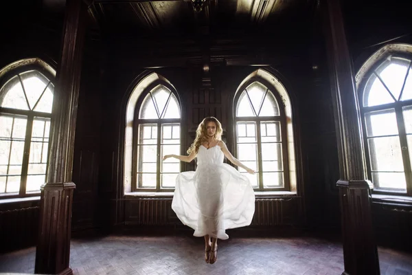 Indoor zomer portret van vrij schattig meisje. Mooie vrouw poseren naast vier fairytale venster in houten kast, oude kasteel van littekens. Bruid springen in witte atlas jurk. Foto heeft een model. — Stockfoto