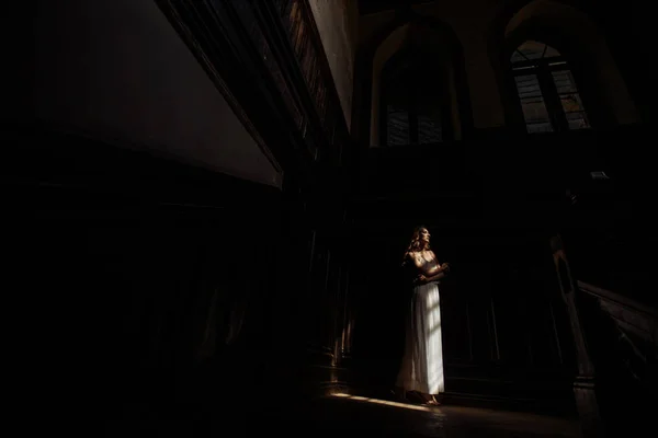 Indoor zomer portret van vrij schattig meisje. Mooie vrouw poseren naast fairytale venster in kast, littekens oude kasteel. Bruid permanent in witte atlas jurk op Bureau trappen. Foto heeft model. — Stockfoto